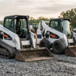 Compact track loader and skid steer parked in an equipment yard in early morning light