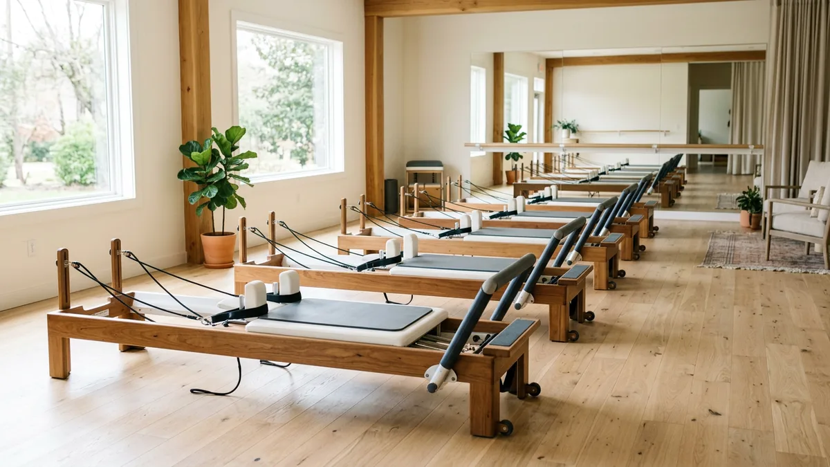 Row of white Pilates reformers lined up on a wood floor in a bright boutique studio