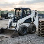 Wheeled skid steer loader parked in a gravel yard in early morning light
