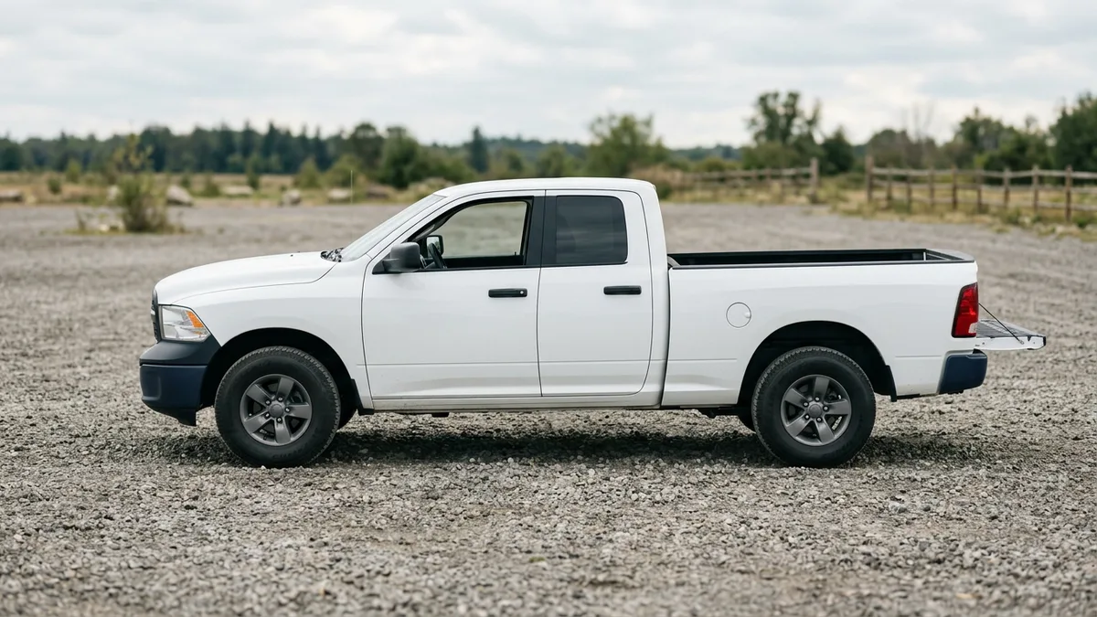 White pickup truck in profile with an empty open cargo bed on a gravel lot